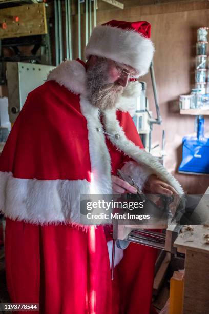 man wearing santa claus costume standing in a workshop, using wood plane. - atelier pere noel photos et images de collection