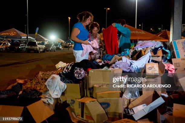 Three women look through a pile of donated clothes at a tent city shelter in a baseball stadium parking lot in Yauco, Puerto Rico on January 14 after...