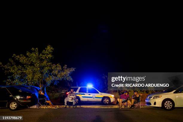 Woman rests on a cot under a blue tarp tied to her car at a tent city shelter in a baseball stadium parking lot in Yauco, Puerto Rico on January 14...