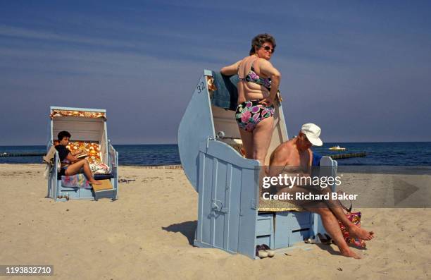 Year after the fall of the Berlin Wall and the end of the Communist Eastern Bloc, sunbathing Germans face away from the wind on the beach at the...