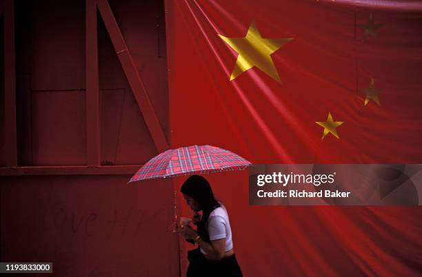 Large banner Chinese flag hangs over a pedestrian on the eve of the handover of sovereignty from Britain to China, on 30th June 1997, in Hong Kong,...