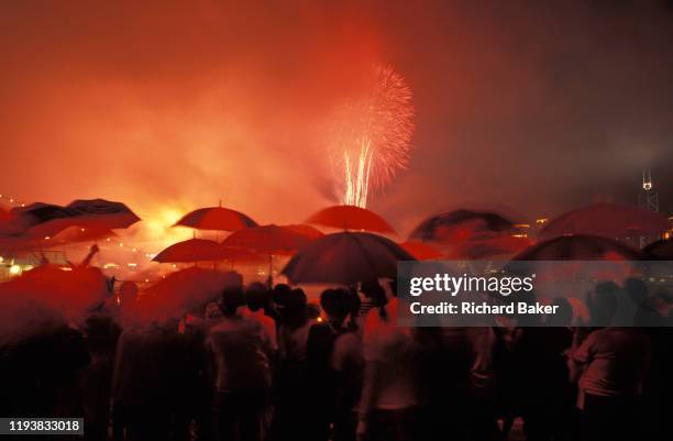 Crowds gather at the stroke of midnight beneath umbrellas to witness the transfer of sovereignty of Hong Kong from the United Kingdom to the Peoples...