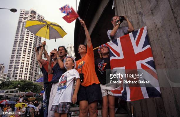 British family hoping to catch a glimpse of passing VIPs, wave Union Jack flags on the eve of the handover of sovereignty from Britain to China, on...
