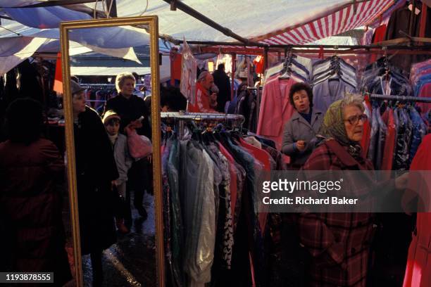 Reflected in a mirror, women shop for clothes at a stall in the covered market in Newport, on 29th November 1985, in Newport, Wales, UK.