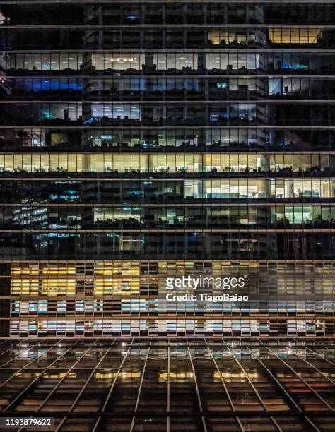 un immeuble de bureaux illuminé la nuit à singapour montrant des contrastes de bleu et de jaune avec des bureaux vides - association of southeast asian nations photos et images de collection