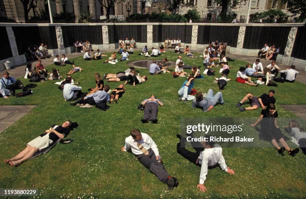 City office workers stretch out over the lush grass during a hot summer lunchtime in Trinity Square in the City of London, on 18th July 1993, in...