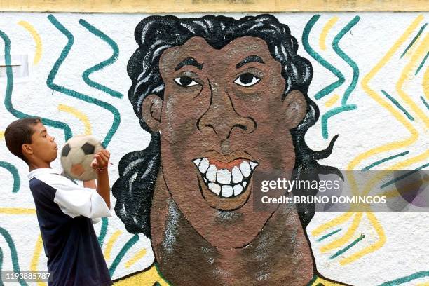 Boy plays with a soccer ball in front of a mural painting which represents Brazilian national soccer team forward Ronaldinho Gaucho in Rio de Janeiro...