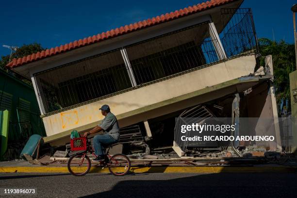 Man rides his bicycle pass by a collapsed house in Guanica, Puerto Rico on January 15 after a powerful earthquake hit the island. - The island is...