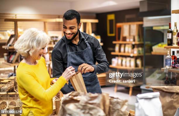 empleado en una tienda de bio comestibles ayudando a un cliente - salesman fotografías e imágenes de stock