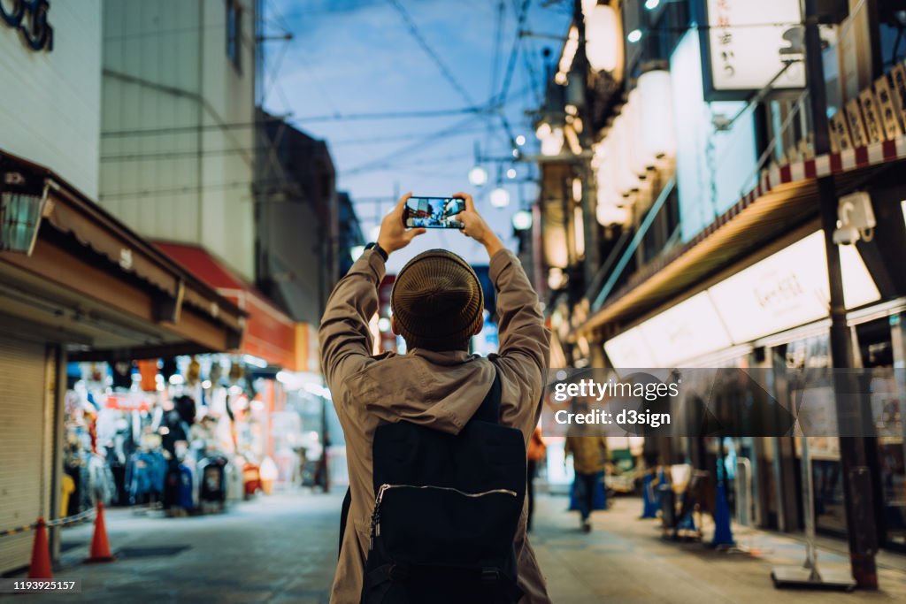 Young Asian male traveller photographing the vitality of local city street scene with smartphone while travelling in Kyoto, Japan