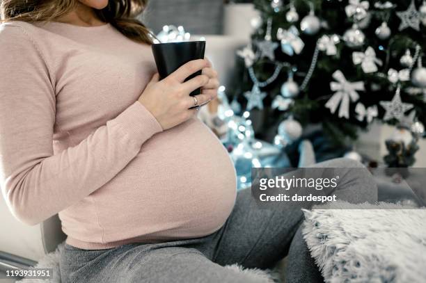 gelukkige zwangere vrouw die koffie drinkt naast de kerstboom - happy new month stockfoto's en -beelden