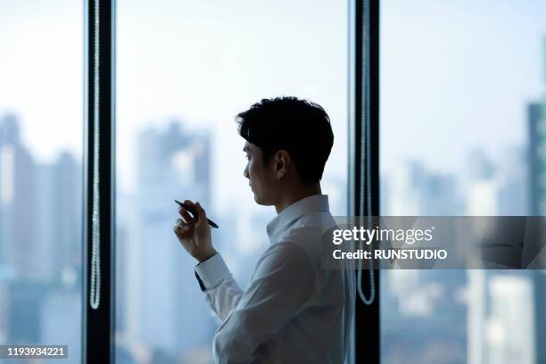 pensive businessman looking through window in office - office japan stock-fotos und bilder