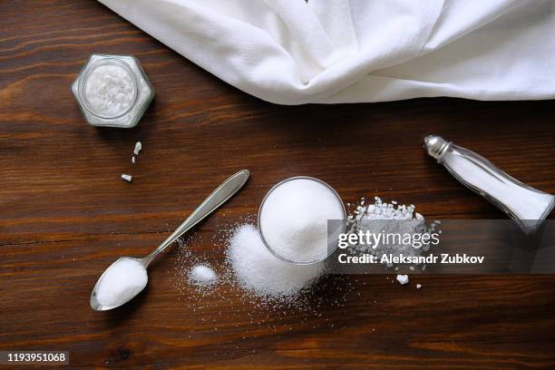 natural seasoning, organic, sea, small and large, white salt in a spoon, in a cup, in a salt shaker, poured on a wooden table. next to a linen towel. the concept of cooking healthy food, cosmetology. - zout smaakstof stockfoto's en -beelden