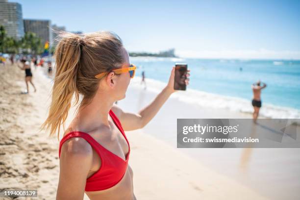 jeune femme prenant la photo de selfie sur la belle plage à honolulu, hawaï, etats-unis - american sunbathing association photos et images de collection