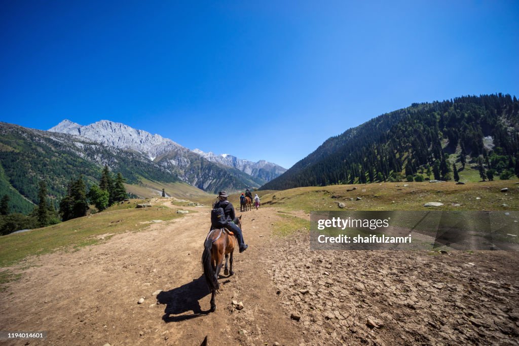 Tourist riding a pony ride over tranquility mountain scene over Sonamarq Valley, Kashmir, India.