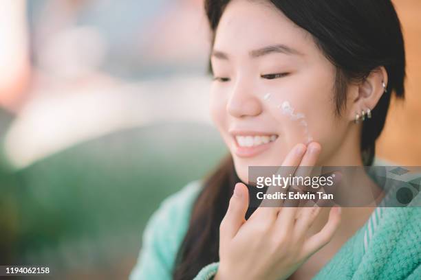 una chica adolescente chino asiático aplicando crema facial hidratante en la mano y la cara - cremas faciales fotografías e imágenes de stock