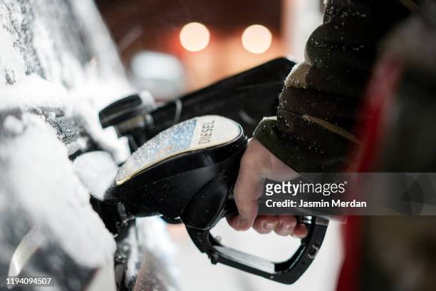 man with fuel hose nozzle tanking car in winter - diesel imagens e fotografias de stock