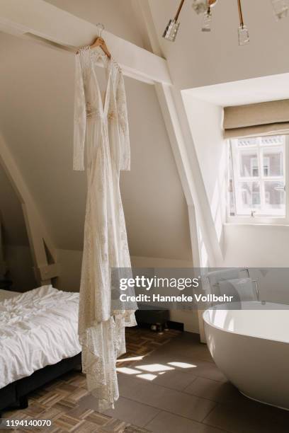 white lace wedding dress hanging in a white room - wedding dress on hanger stock pictures, royalty-free photos & images