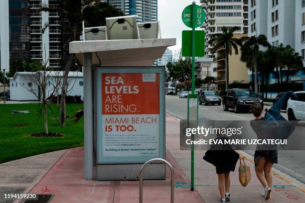 People walk past a billboard about Miami Beach City initiatives regarding sea levels rise at Collins Ave in Miami Beach on January 17, 2020. - Dozens...