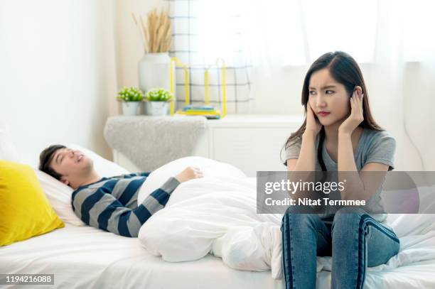 young asian couple in bed.  young man snoring and woman can't sleep, covering ears with hand for snohere noise at home in bedroom. - schnarchen mann stock-fotos und bilder