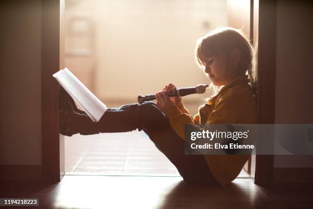 girl (6-7) sitting in a doorway in a home learning to play a musical recorder - recorder musical instrument stock pictures, royalty-free photos & images