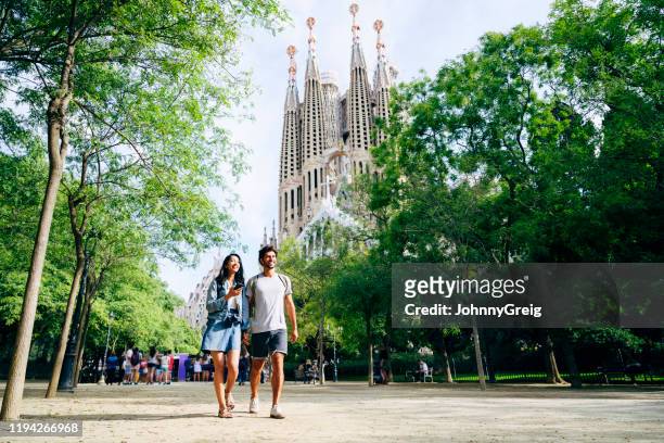 smiling vacationers holding hands and walking in barcelona - sagrada família imagens e fotografias de stock