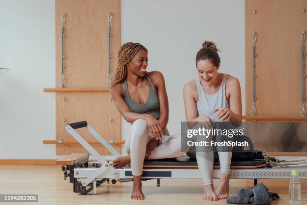 girlfriends sitting on piiates reformer and chatting - pilates machine stock pictures, royalty-free photos & images
