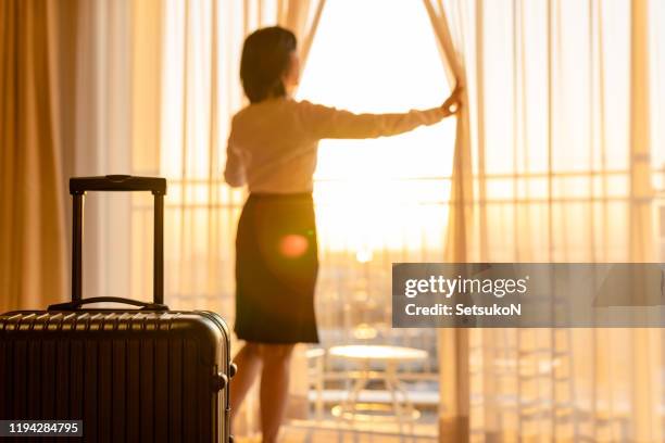 asian businesswoman pulling the curtains to see the view - business woman suitcase stock pictures, royalty-free photos & images