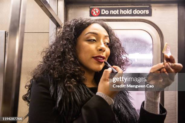 a confident dominican woman putting on lipstick on subway - showus makeup stock pictures, royalty-free photos & images