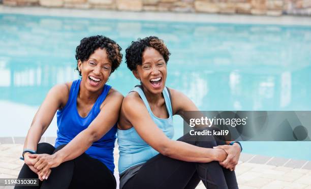 identical twins sitting on yoga mats by pool, laughing - twin stock pictures, royalty-free photos & images