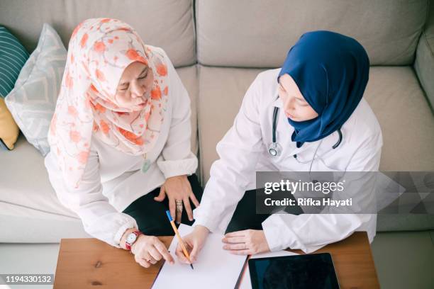 desde arriba - paciente decirle al joven doctor acerca de su sentimiento y el médico grabarlo - hiyab fotografías e imágenes de stock