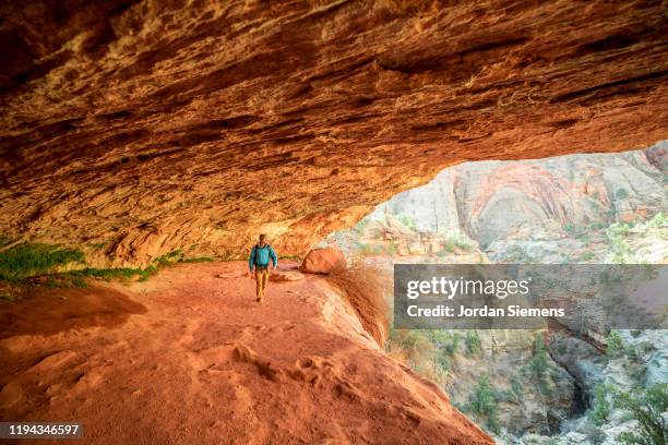 a man hiking under a scenic trail under a giant overhang - st george utah stock pictures, royalty-free photos & images