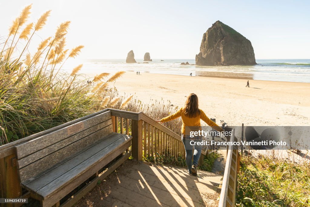 Woman looking at Haystack rock from a wooden footpath. Cannon Beach, Oregon, USA.