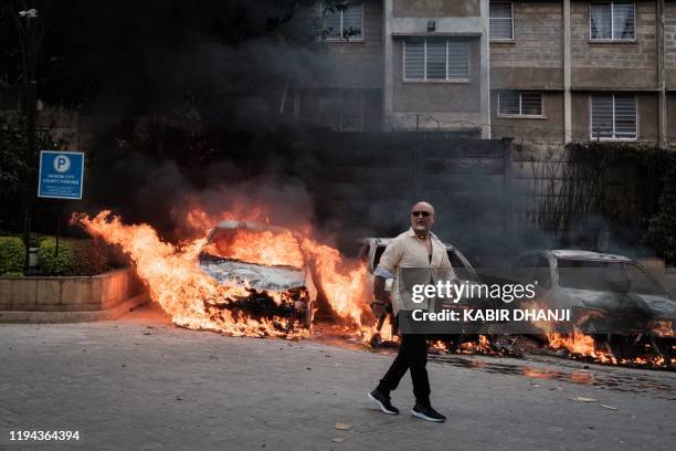 Man passes in front of burning cars that exploded at the entrance of DusitD2 hotel in Nairobi, Kenya, on January 15 after a blast followed by a gun...