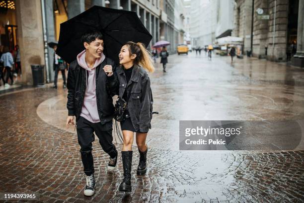 happy young couple walking in the rain - sharing umbrella stock pictures, royalty-free photos & images
