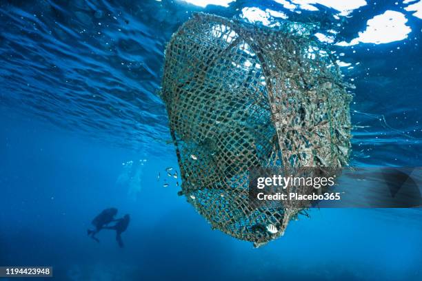 el pez ghost net abandonado agrega el dispositivo que contamina el océano cerca de buceadores - commercial fishing net fotografías e imágenes de stock