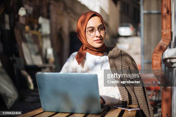 junge frau sitzt im bürgersteig-café und benutzt laptop - islam stock-fotos und bilder