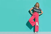Stylish Woman In Pink Wide Legs Trousers, Sneakers And Striped Blouse Is Posing On One Leg