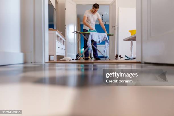 man ironing in messy living room - ironing board imagens e fotografias de stock