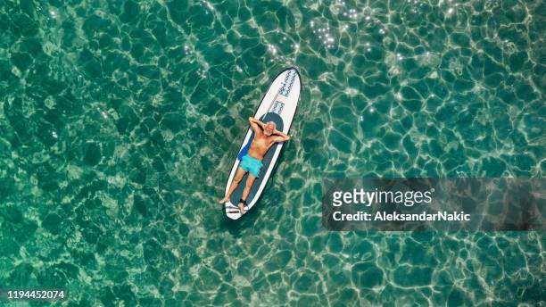 senior man relaxing on a paddleboard - aerial beach view sunbathers stock pictures, royalty-free photos & images