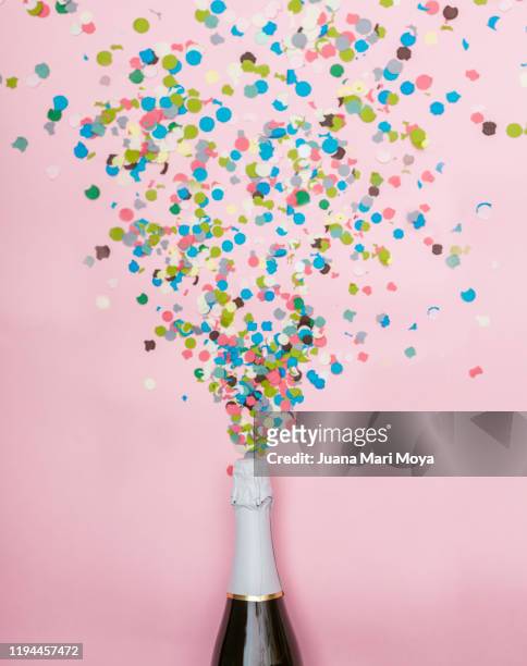 minimalist photograph of a bottle of champagne, confetti comes out of it.  celebration and new year concept - new year new you 2019 stock-fotos und bilder