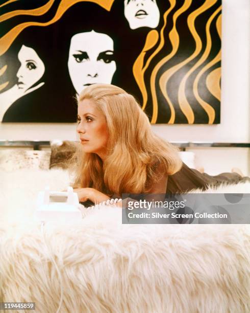 Catherine Deneuve, French actress, laying on a fur surface, with an artwork hanging on the wall behind her, in a publicity still issue for the film,...