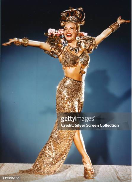 Carmen Miranda , Portuguese-born Brazilian singer, actress and dancer, wearing a long gold sequinned split skirt, with a matching bra-top and various...