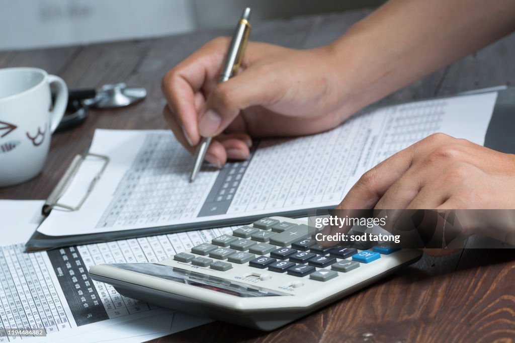 Closeup of a young caucasian healthcare professional wearing a white coat calculates on an electronic calculator