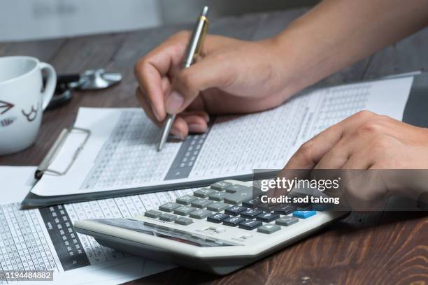 closeup of a young caucasian healthcare professional wearing a white coat calculates on an electronic calculator - affordability stock pictures, royalty-free photos & images