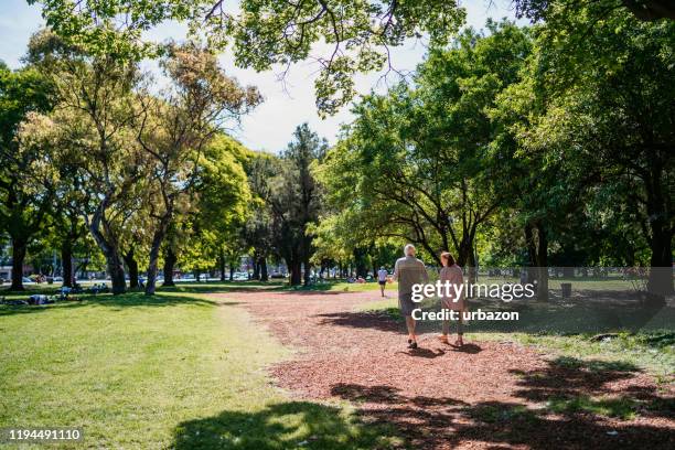 senior couple walking in public park - park footpath stock pictures, royalty-free photos & images