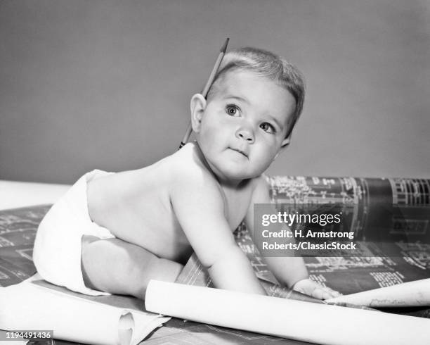 1960s PROFESSIONAL DESIGNER BABY WEARING CLOTH DIAPER PENCIL BEHIND EAR LOOKING UP CRAWLING WORKING ON BUILDING BLUEPRINTS