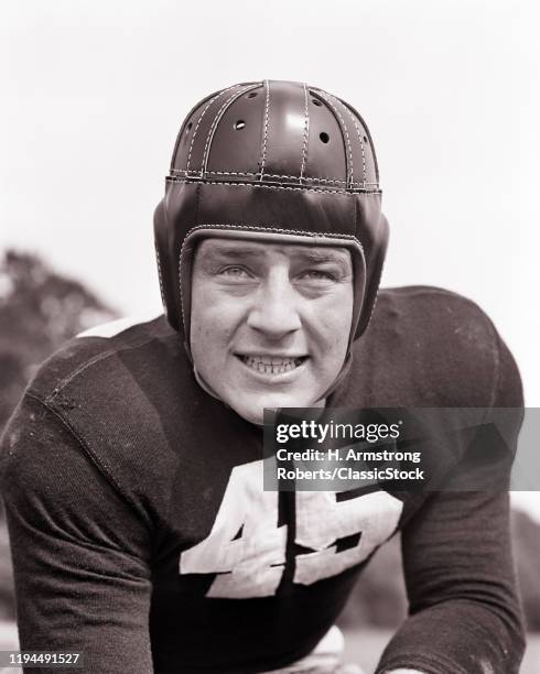 1940s YOUNG MAN FOOTBALL PLAYER WEARING LEATHER PROTECTIVE HELMET GRITTING TEETH IN THREATENING EXPRESSION LOOKING AT CAMERA