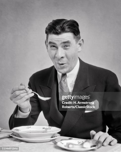 1930s MAN WEARING SUIT AND TIE EATING A BOWL OF SOUP MAKING A FUNNY FACIAL EXPRESSION AS SOUP TOO HOT OR DELICIOUS OR HORRIBLE