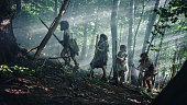 Tribe of Hunter-Gatherers Wearing Animal Skin Holding Stone Tipped Tools, Explore Prehistoric Forest in a Hunt for Animal Prey. Neanderthal Family Hunting in the Jungle or Migrating for Better Land